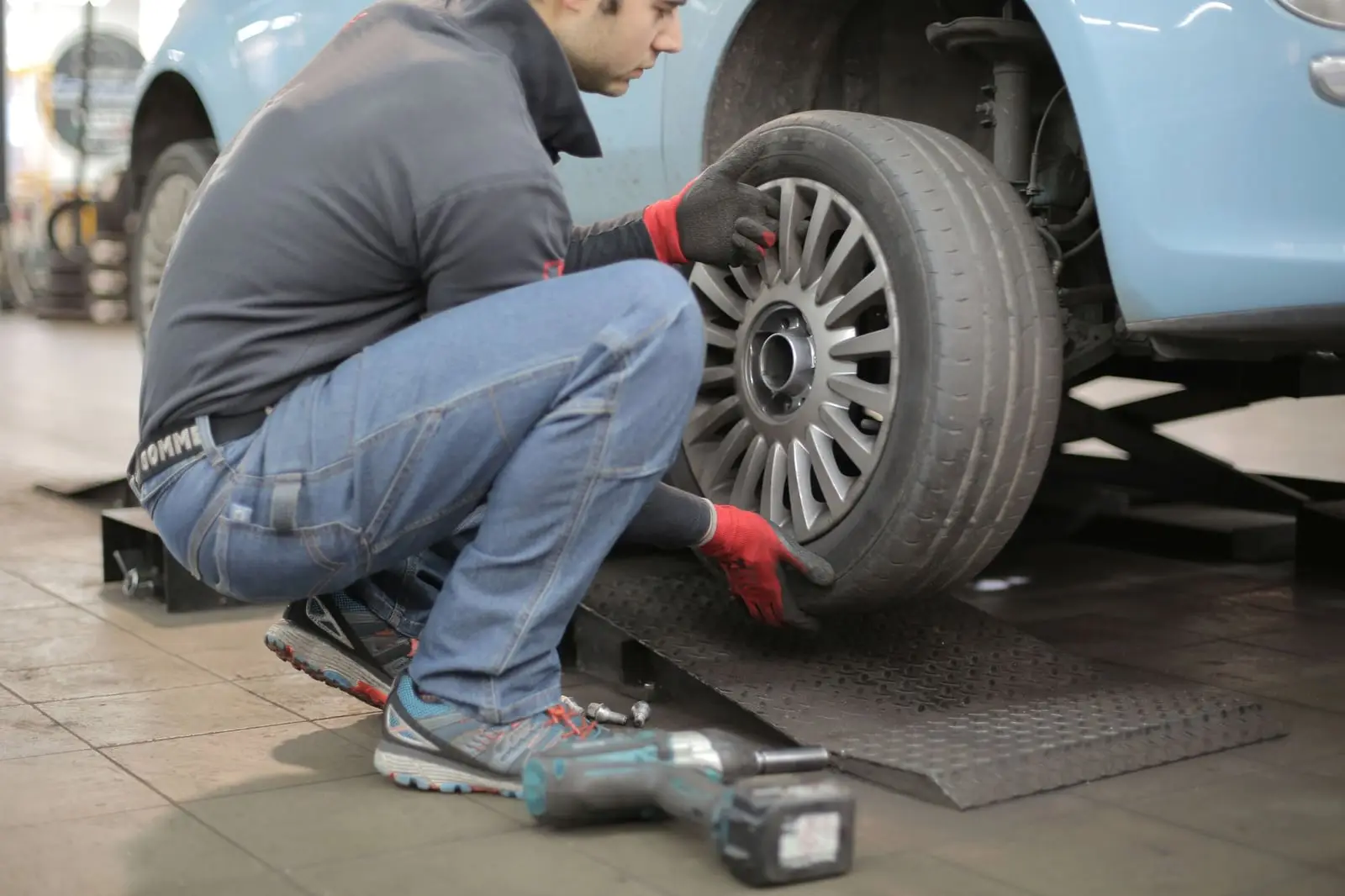 Mechaniker montiert ein Rad an einem angehobenen Kleinwagen, daneben ein Schlagschrauber