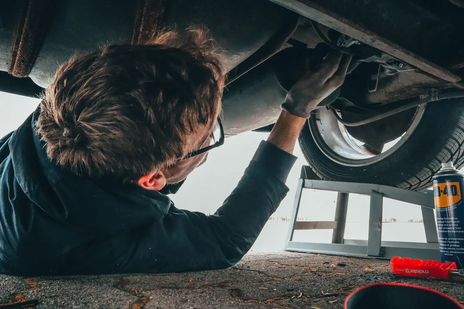 Mechaniker liegt unter einem aufgebockten Auto und prüft den Unterboden
